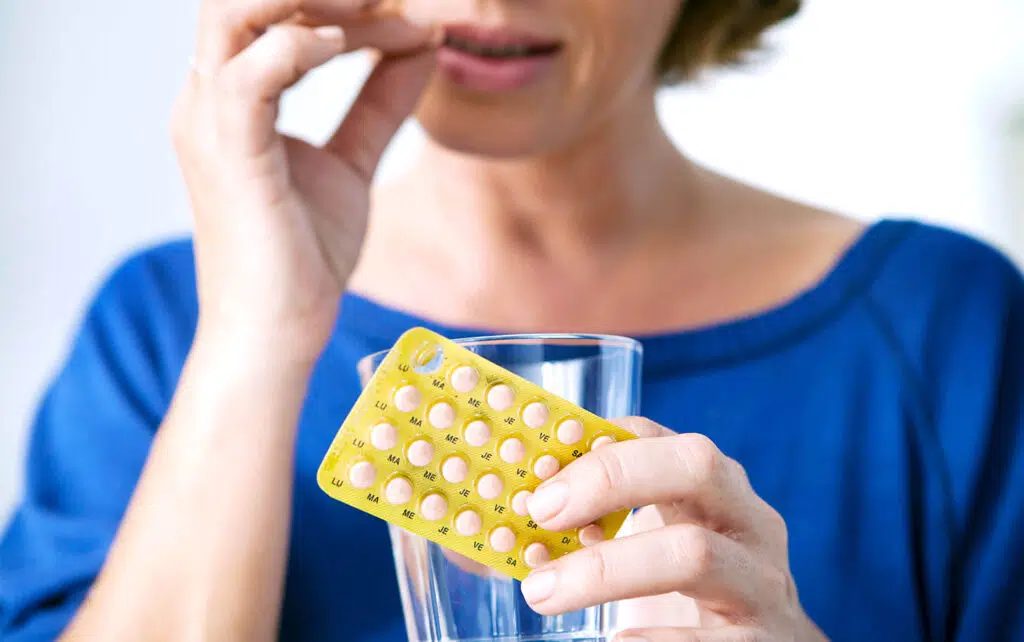 Een vrouw die aan hormoontherapie doet en die een pillen strip vast heeft met haar linker hand en met haar rechter hand een van de pillen in haar mond doet.