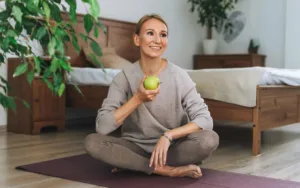 Een vrouw die op een yoga matje zit met een appel in de hand | Voel je goed tijdens de overgang!