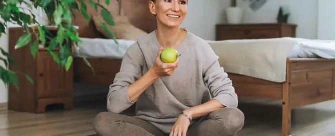 Een vrouw die op een yoga matje zit met een appel in de hand | Voel je goed tijdens de overgang!